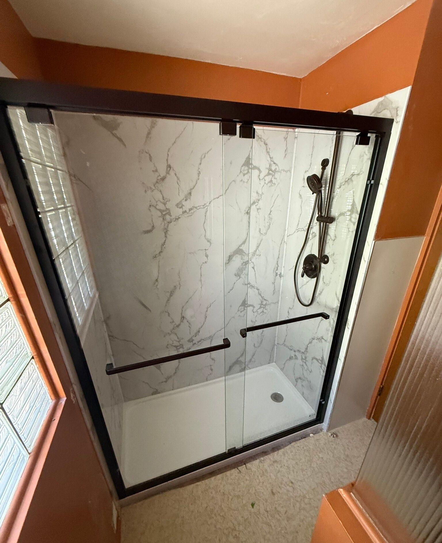A black-framed glass tub-to-shower conversion with marble tile